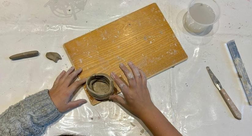 Mani di un bambino che modella l'argilla su una tavoletta di legno, un'attività del laboratorio creativo utile per sfogare la rabbia e migliorare la manualità