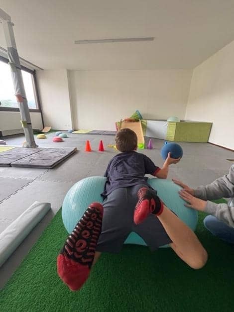 Ergoterapista che assiste un bambino durante un esercizio di coordinazione e forza su una palla terapeutica per migliorare la percezione corporea