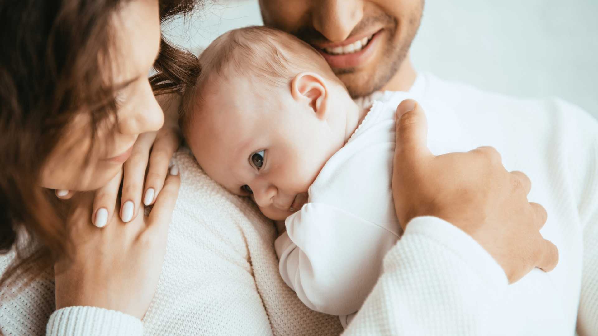 Genitori che sorreggono con cura il capo e la schiena di un neonato, illustrando le buone pratiche di sicurezza suggerite dal pediatra a Paradiso