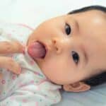 Neonato sdraiato mentre un pediatra o un genitore controlla delicatamente l'interno della bocca e la mobilità della lingua