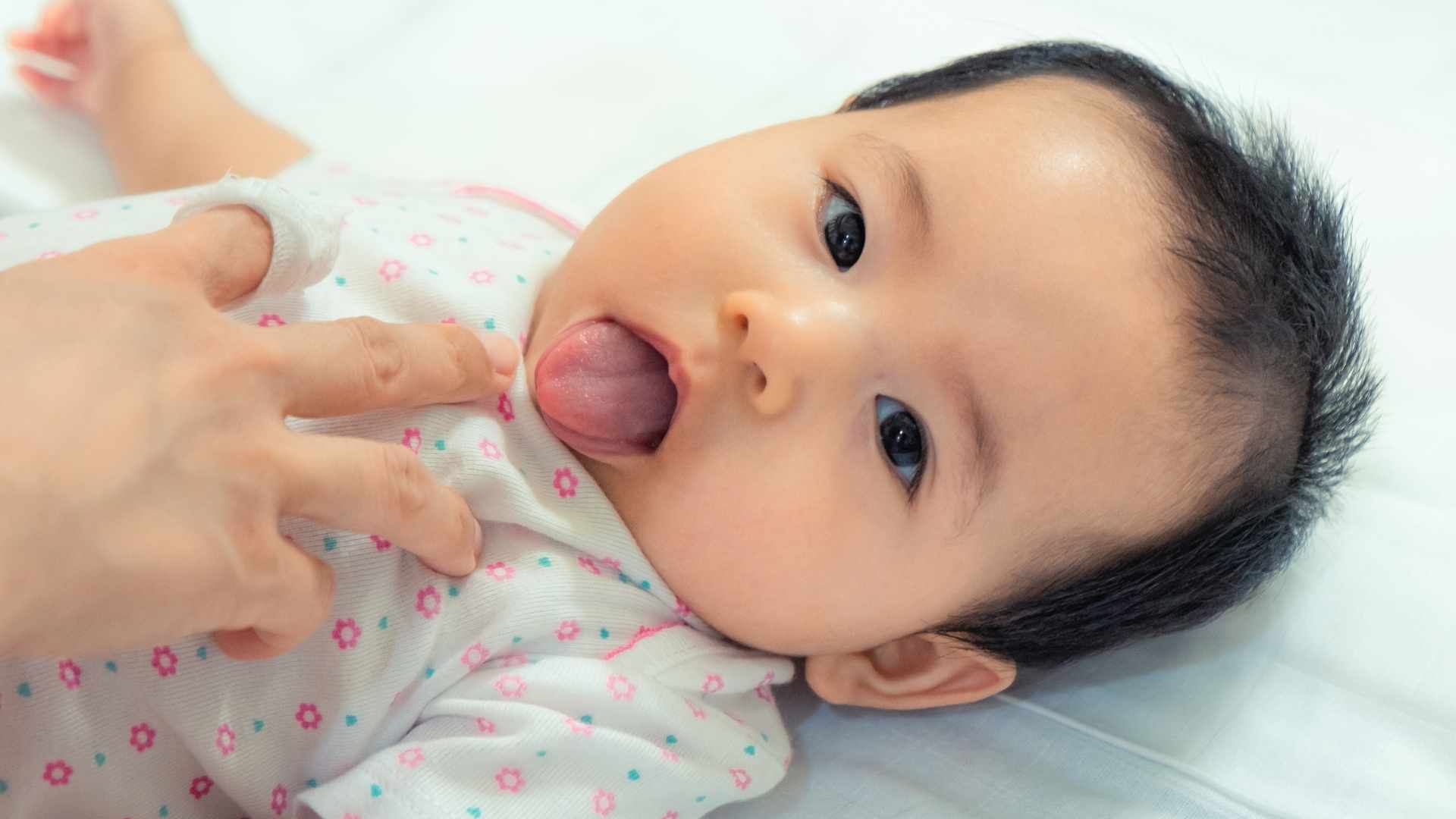 Neonato sdraiato mentre un pediatra o un genitore controlla delicatamente l'interno della bocca e la mobilità della lingua