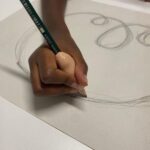 Primo piano della mano di un bambino che utilizza un adattatore ergonomico per impugnare correttamente una matita e disegnare cerchi su un foglio di carta.